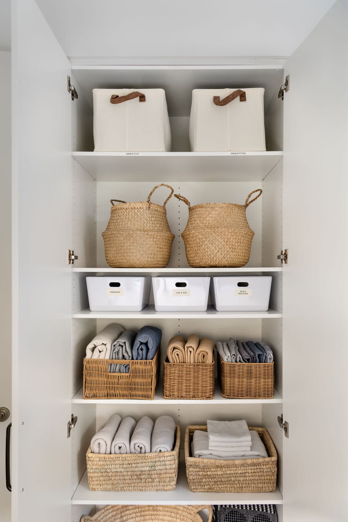 White shelving holding two tall fabric bins, seagrass baskets, labelled white tubs, and shoes in pairs on the lower shelf.