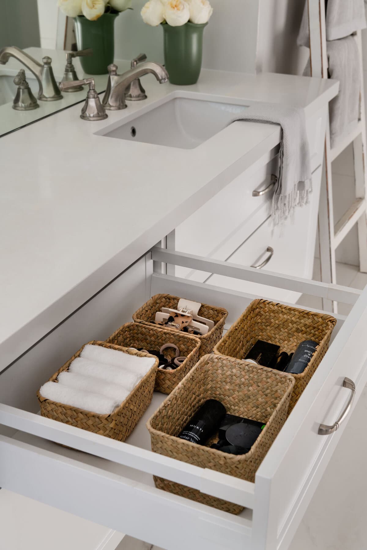 An open drawer under a stone benchtop holding woven baskets of rolled white towels and folded dark linen.